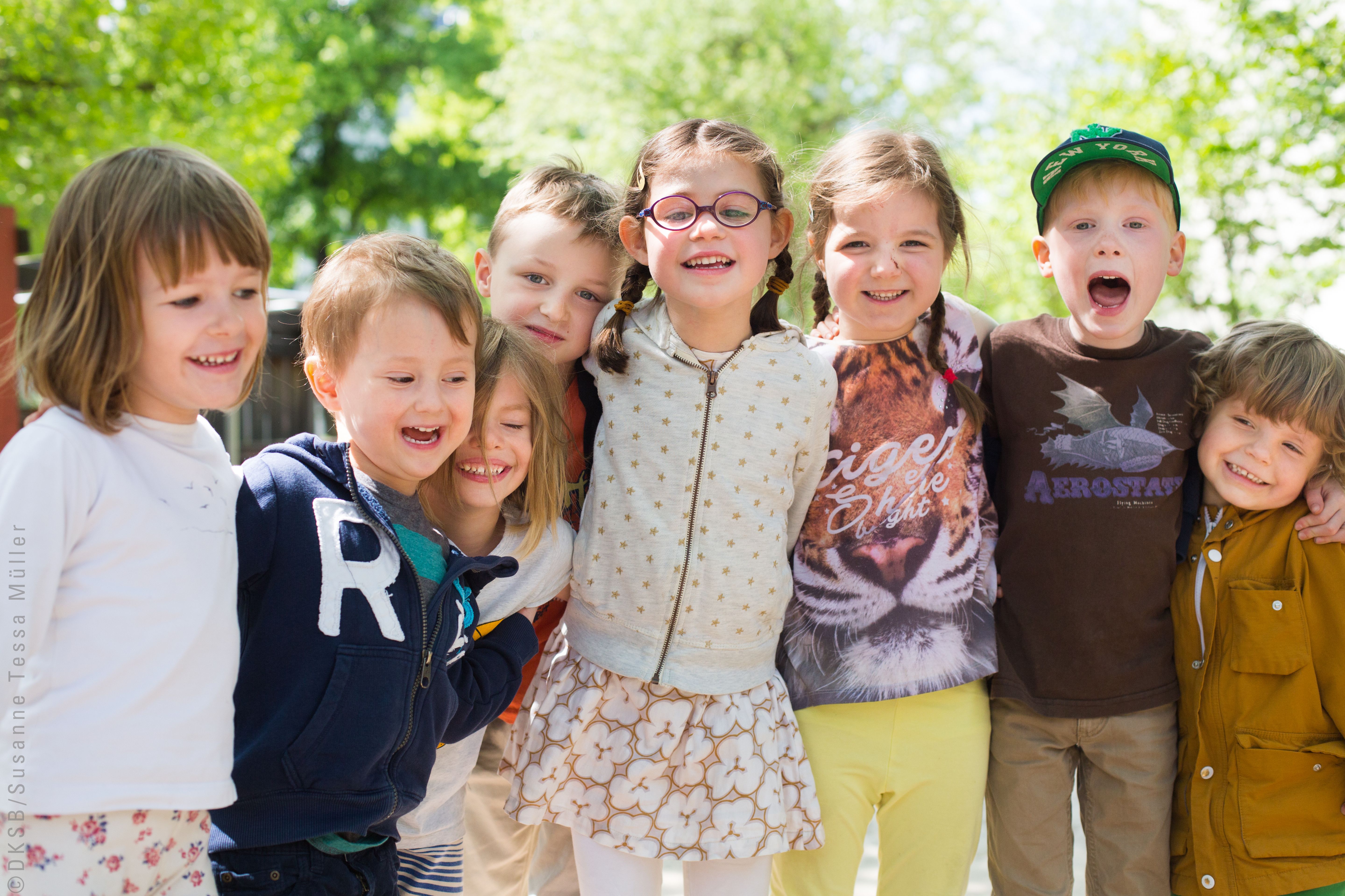 Eine Gruppe fröhlicher Kinder lächelt und posiert gemeinsam im Freien unter strahlendem Sonnenschein.