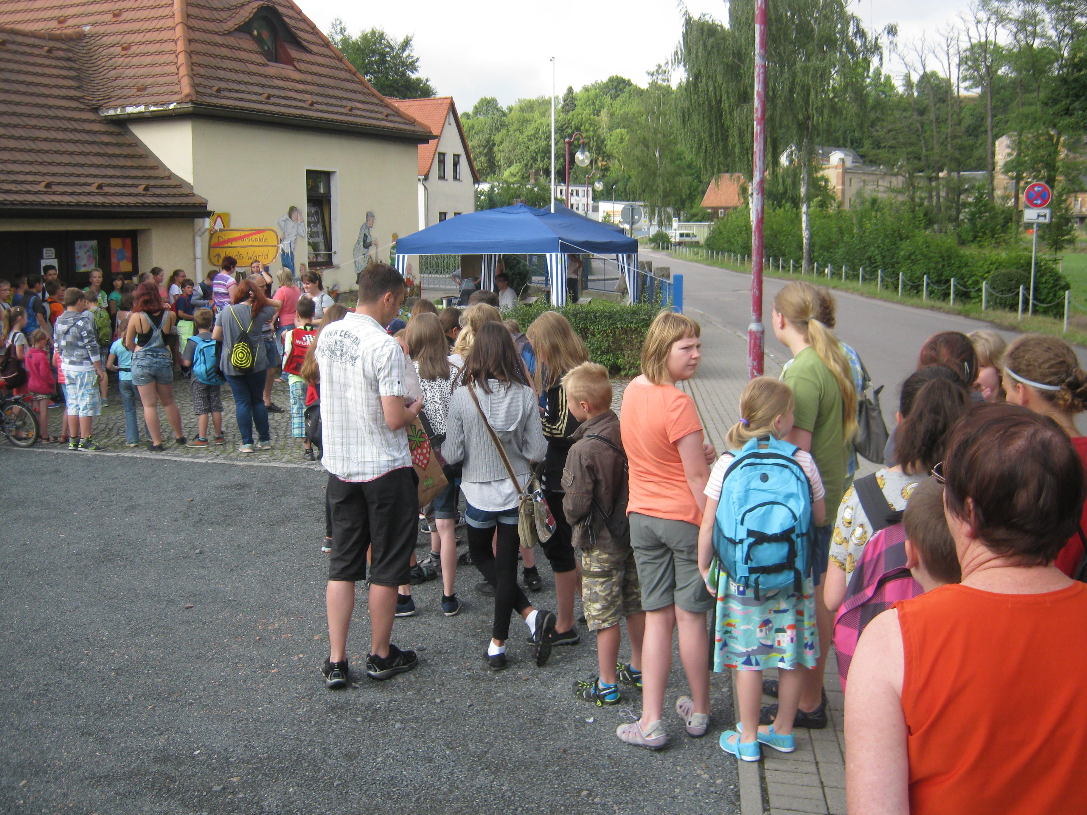 Kinder stehen in einer langen Schlange vor einem Veranstaltungszelt, voller Vorfreude auf die Aktivitäten in der Kinderstadt.