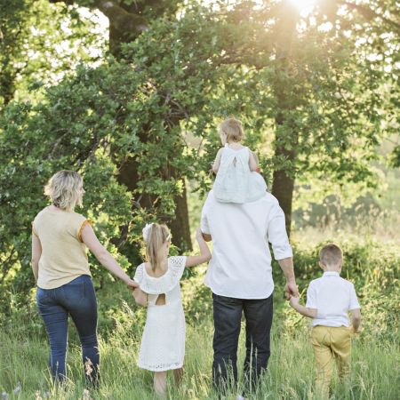 Eine Familie mit zwei Kindern genießt einen sonnigen Tag in der Natur, während sie zusammen in Richtung eines Baumes spazieren.