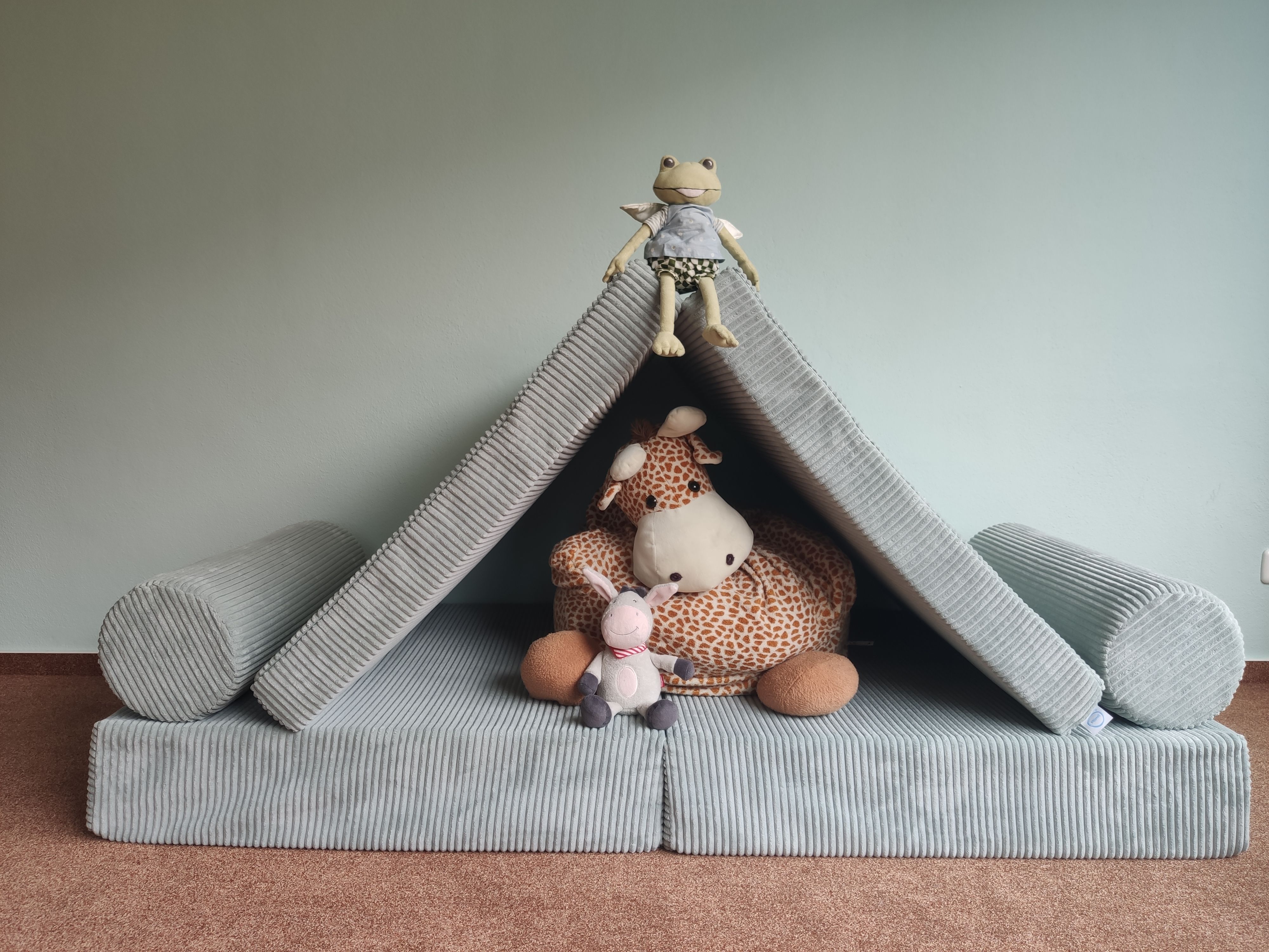 Ein gemütliches Kissen-Fort ist mit einem Stofftier und einer Giraffe zum Spielen dekoriert.