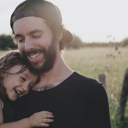 Ein glücklicher Vater lächelt, während er sein lachendes Kind in einer sonnigen Wiese hält.